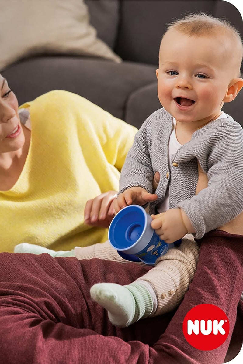 Dziecko siedzące na kolanach dorosłego i trzymające niebieski kubek NUK Mini Magic Cup.