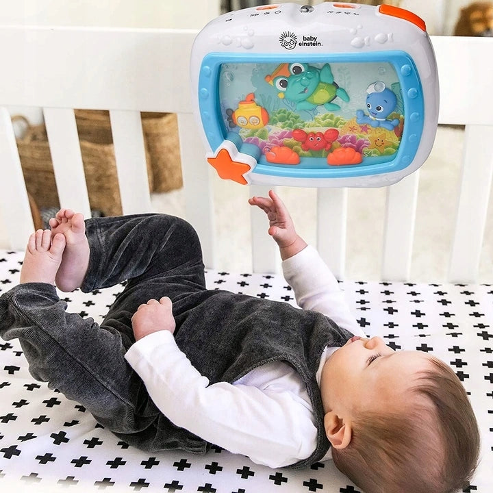 Niemowlę leży w białym łóżeczku pod pozytywką Baby Einstein Morskie Sny z figurkami morskich zwierząt.