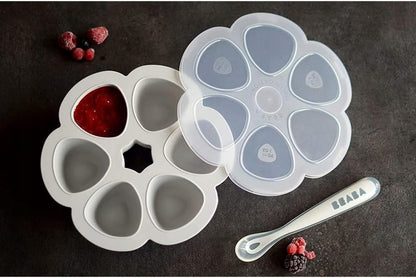 Szara forma Béaba 912806 z musem w jednym zagłębieniu, odłożoną pokrywką, owocami i łyżeczką.