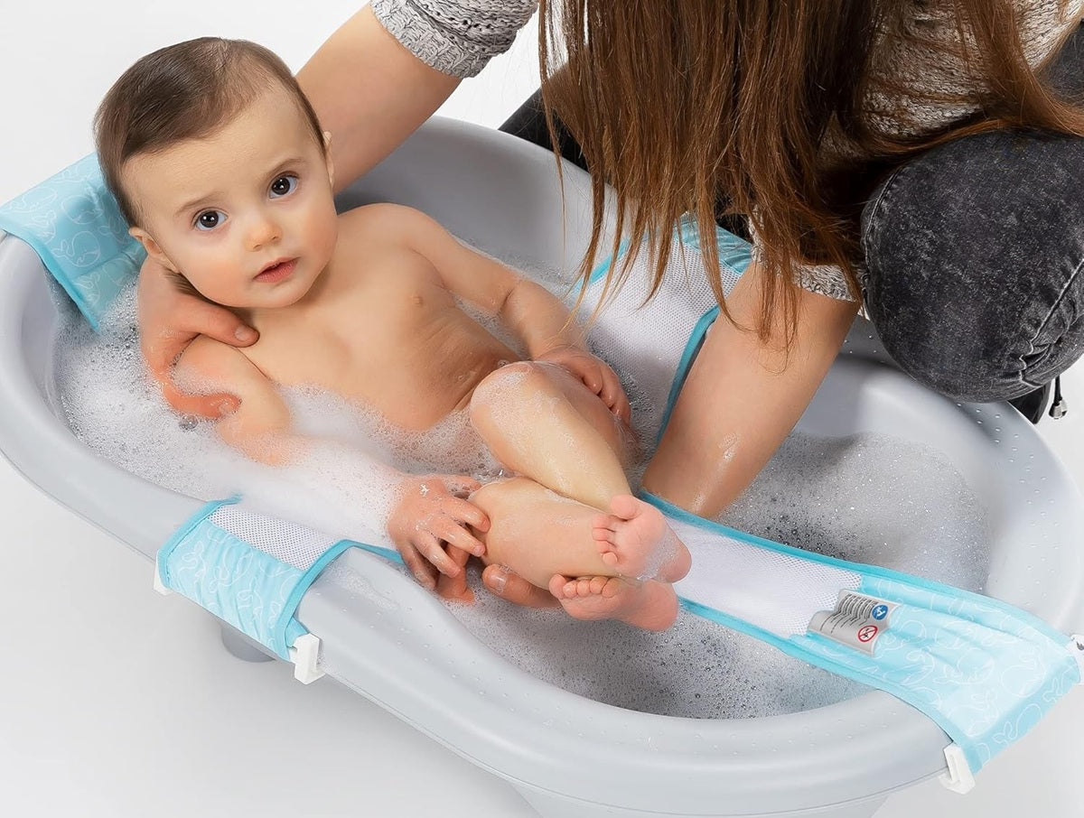 Dorosła osoba podtrzymująca dziecko podczas kąpieli na siatce Reer MyHappyBath Sling 76072 w szarej wanience.