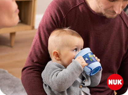 Dziecko trzymające niebieski kubek NUK Mini Magic Cup przy ustach na kolanach dorosłego.