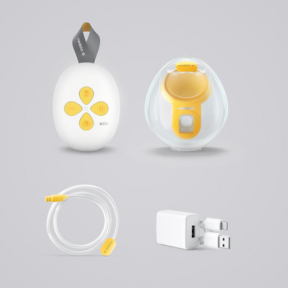 Panel i jedna muszla Medela Solo Hands-Free, przewód oraz zasilacz rozłożone na szarym tle.