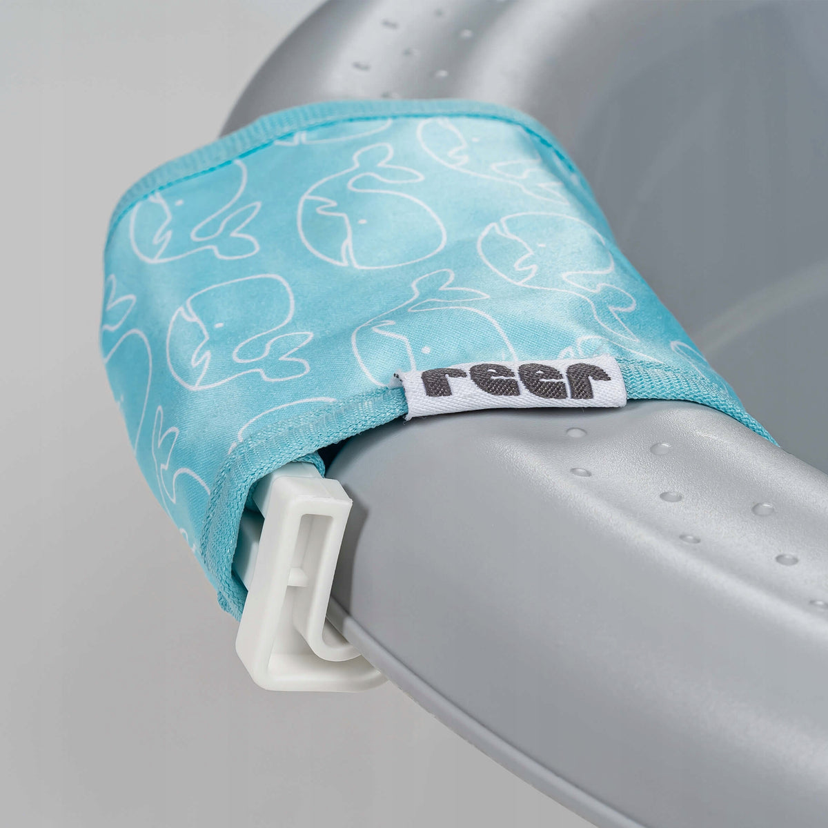 Zbliżenie białej klamry i niebieskiego brzegu siatki Reer MyHappyBath Sling 76072 ze wzorem wielorybów.