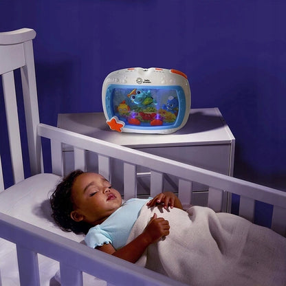 Pozytywka Baby Einstein Morskie Sny stoi na szafce przy dziecięcym łóżku w pokoju o niebieskim oświetleniu.